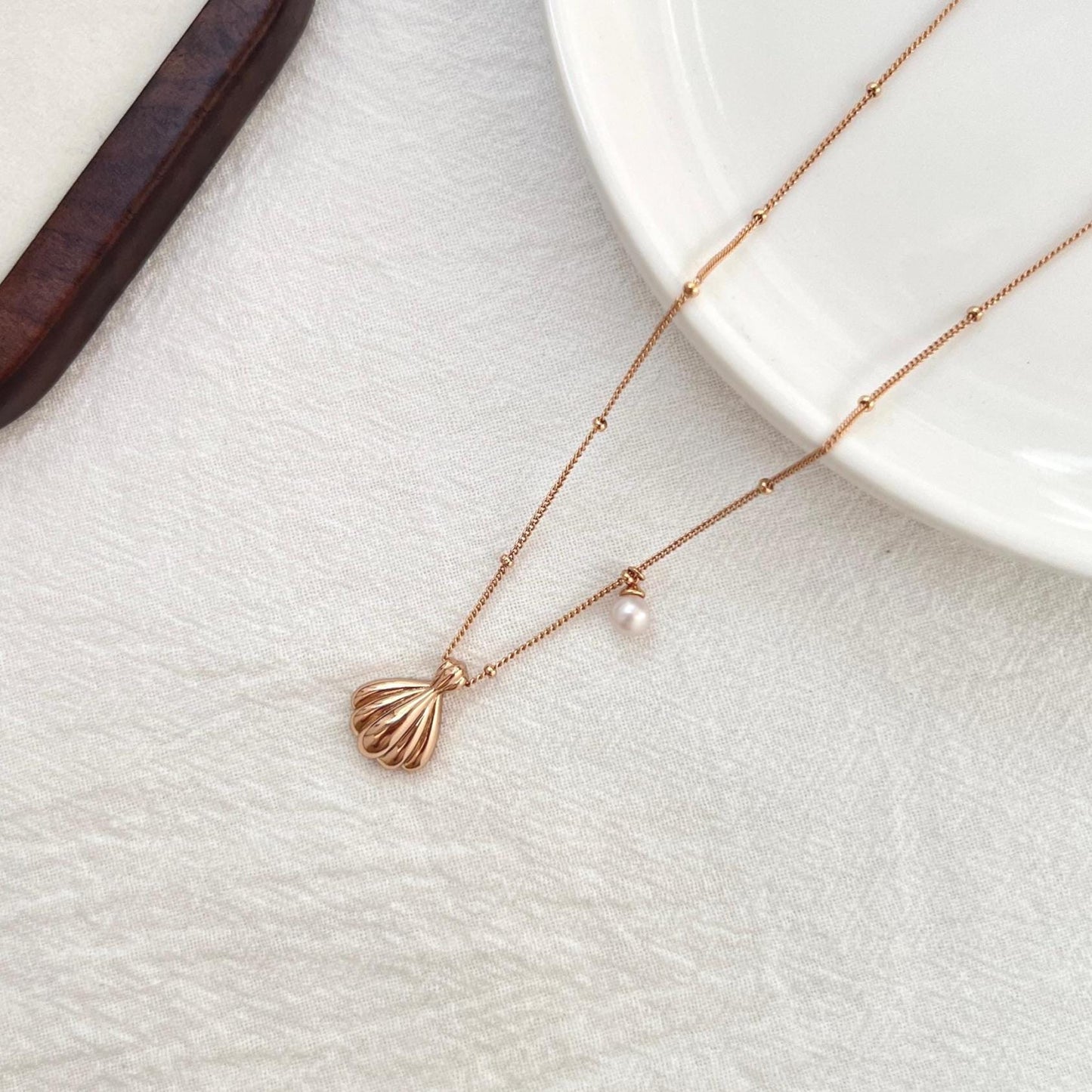 Front view of 18K gold shell pendant with freshwater pearl charm on a delicate chain