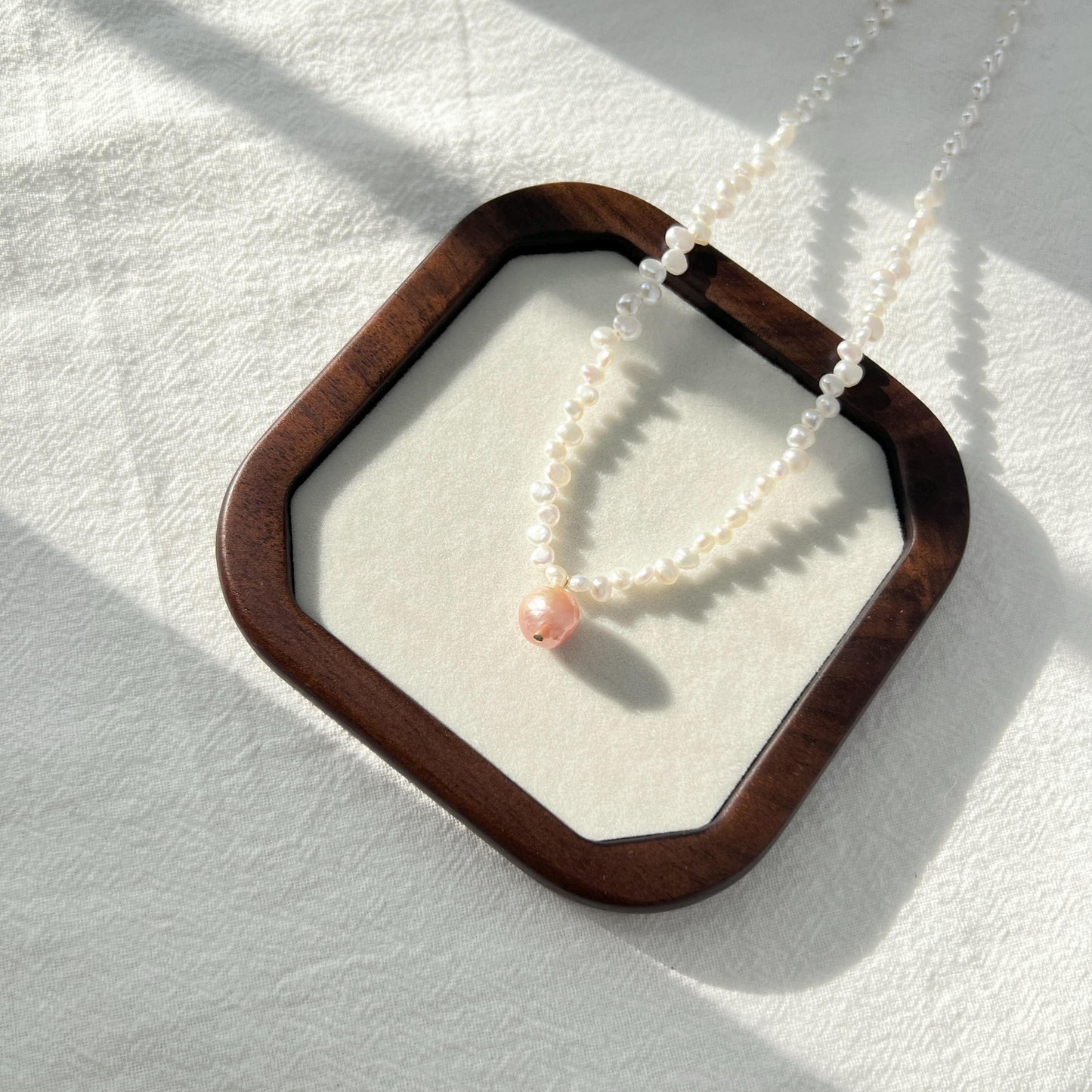 Pearl necklace with a pink bead on a white background