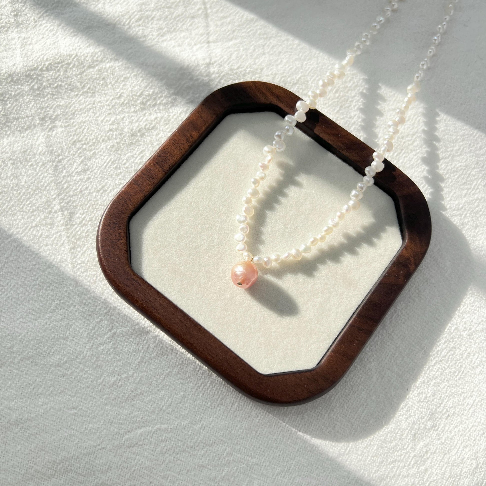 Pearl necklace with a pink bead on a white background