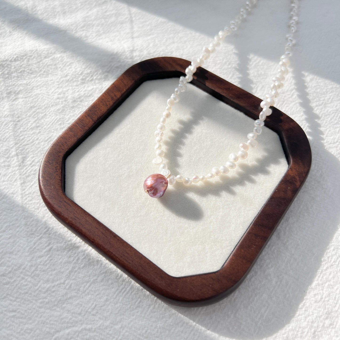 Necklace with a pink pendant on a wooden stand against a white background