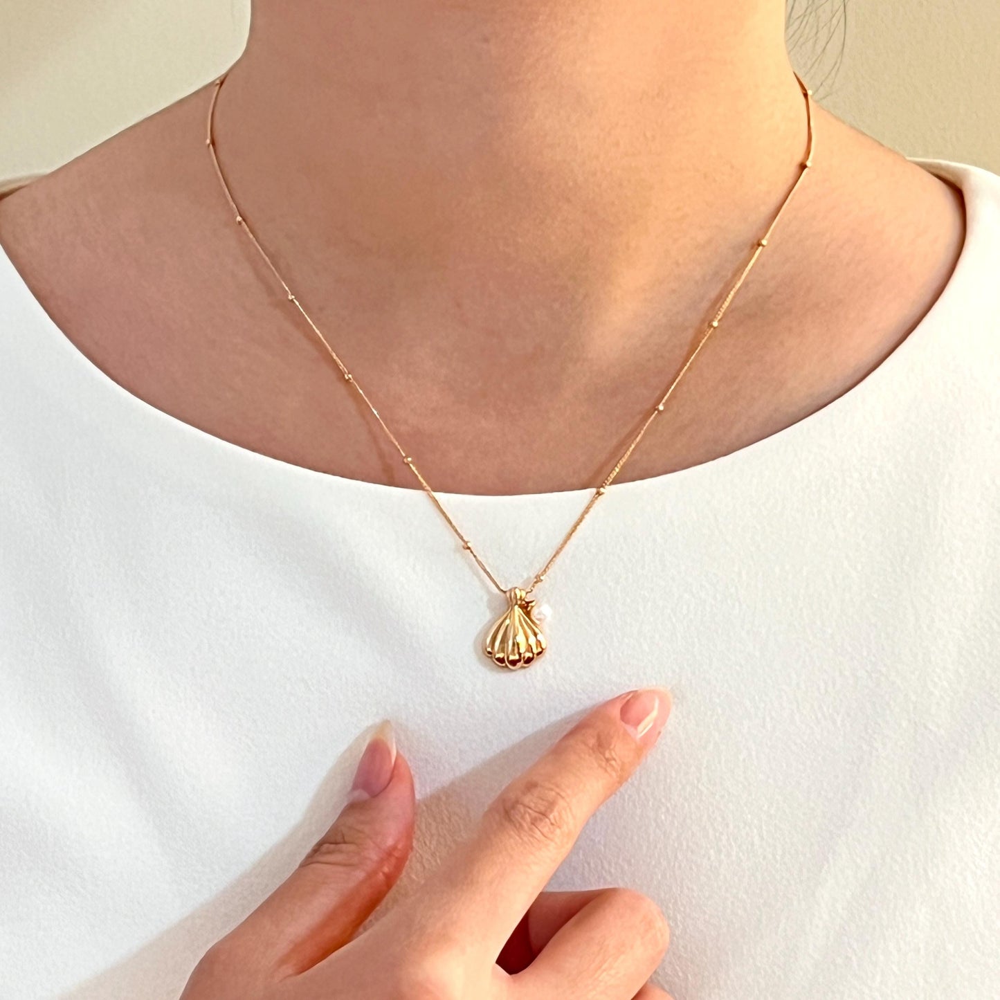 Model wearing 18K gold shell freshwater pearl charm necklace, styled elegantly