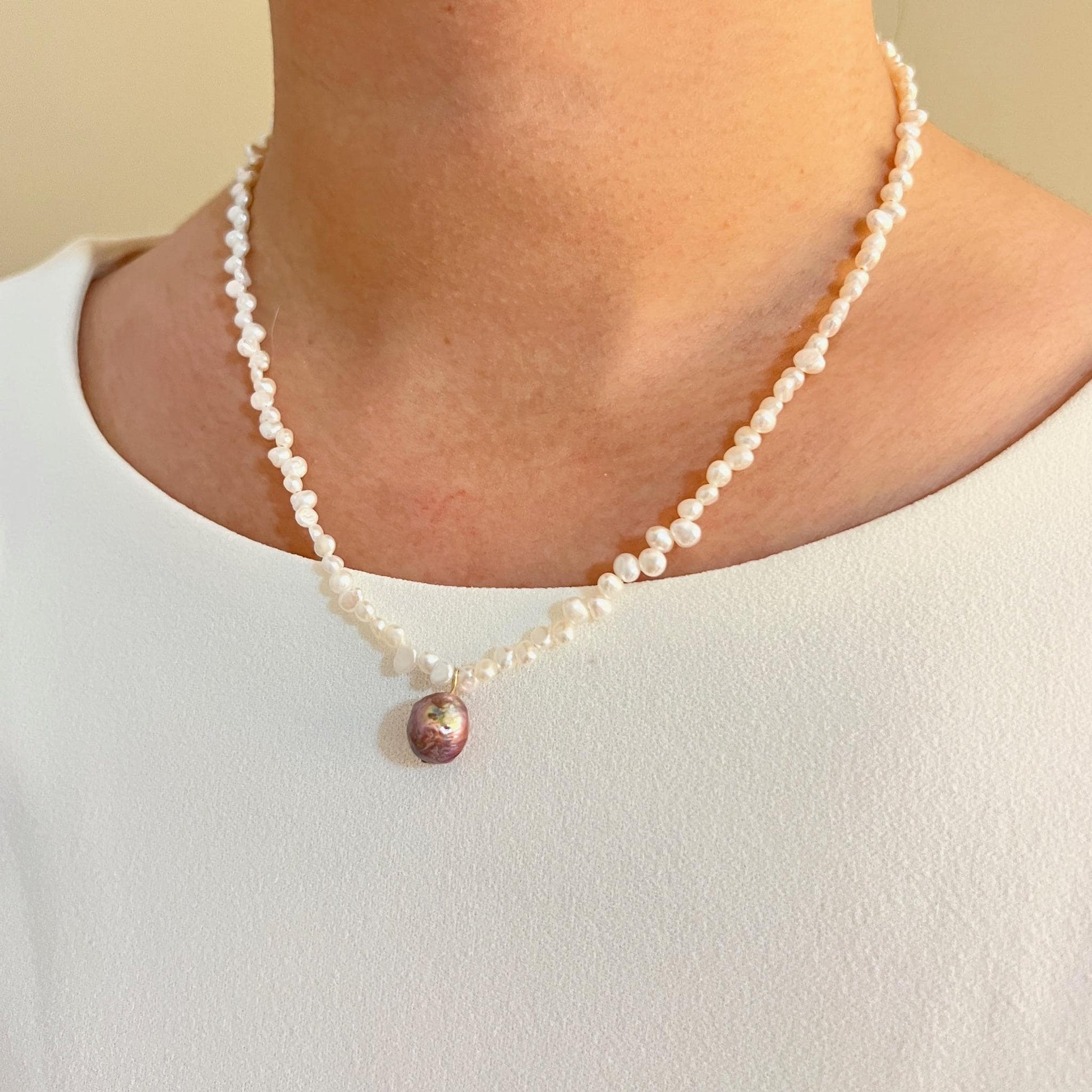 Pearl necklace with a pink pendant worn by a person against a neutral background