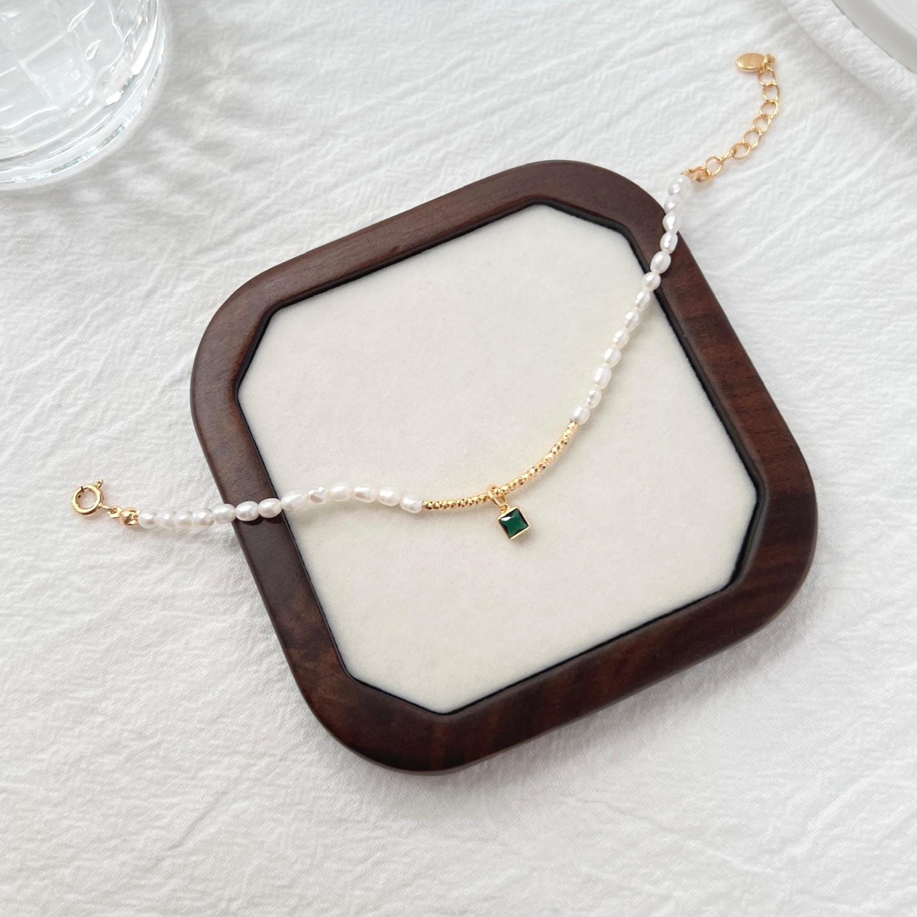 Side view of 18K gold baroque pearl bracelet featuring a green zircon charm