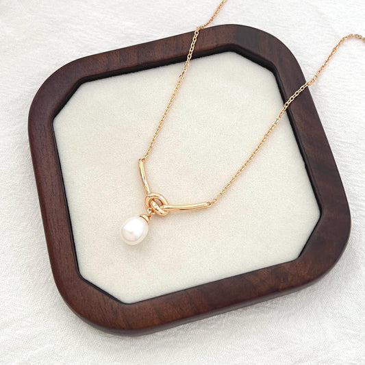Close‑up of the rope knot design and natural freshwater pearl on a 18K gold plated necklace, delicate bridal jewelry.