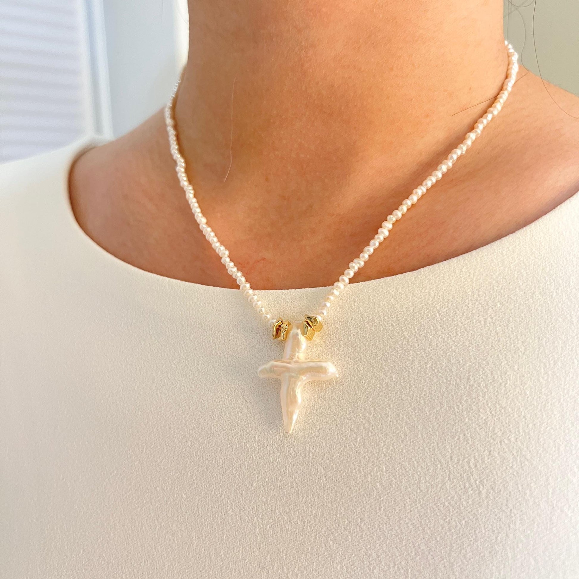 Pearl necklace with a gold pendant worn by a person against a neutral background