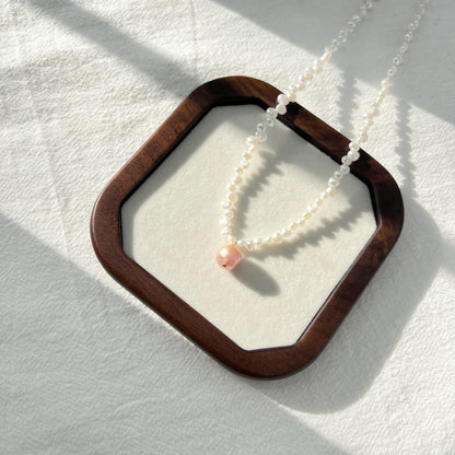Pearl necklace with a pink bead on a white background