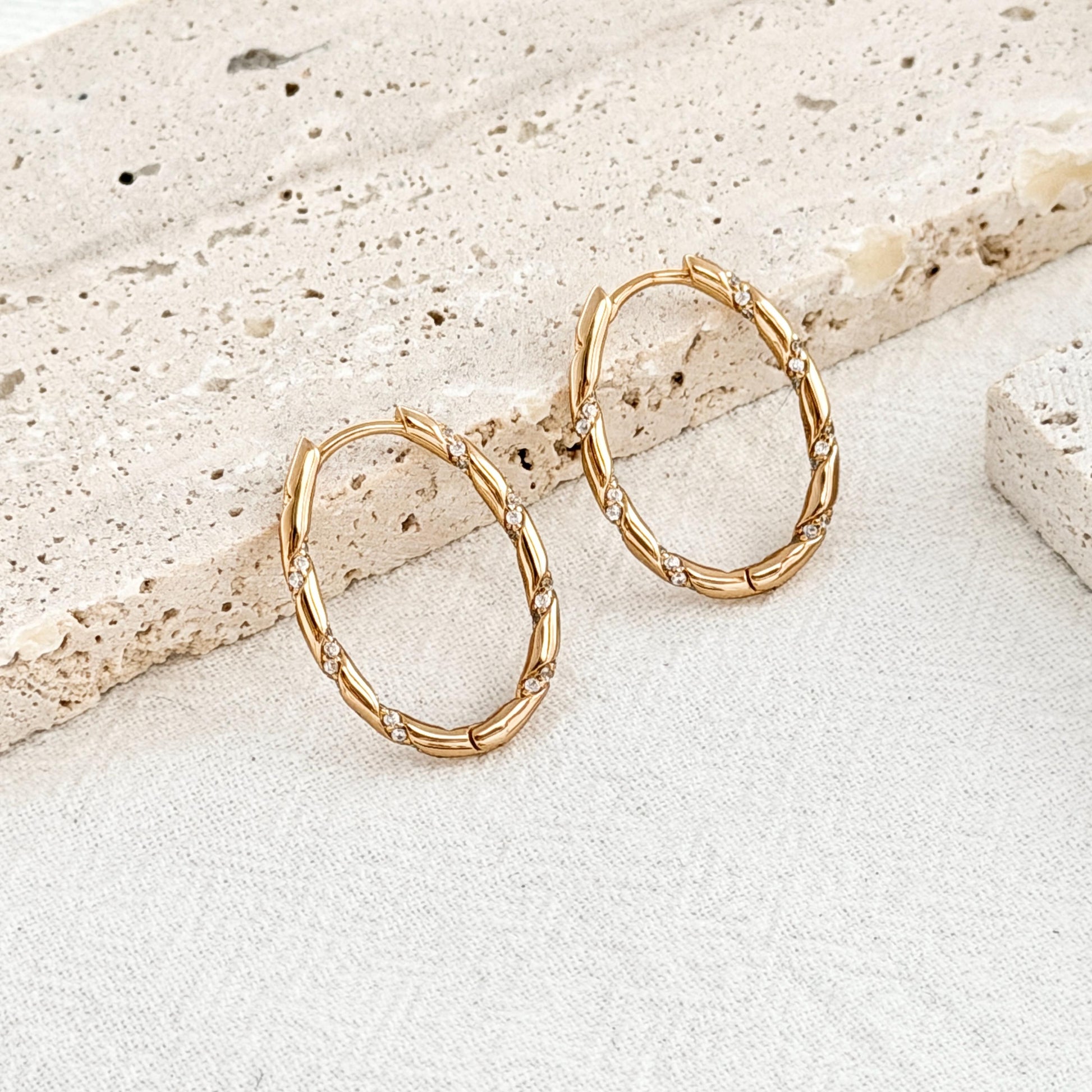 close up of 18k gold oval hoop earrings twisted rope design with sparkling cz accents
