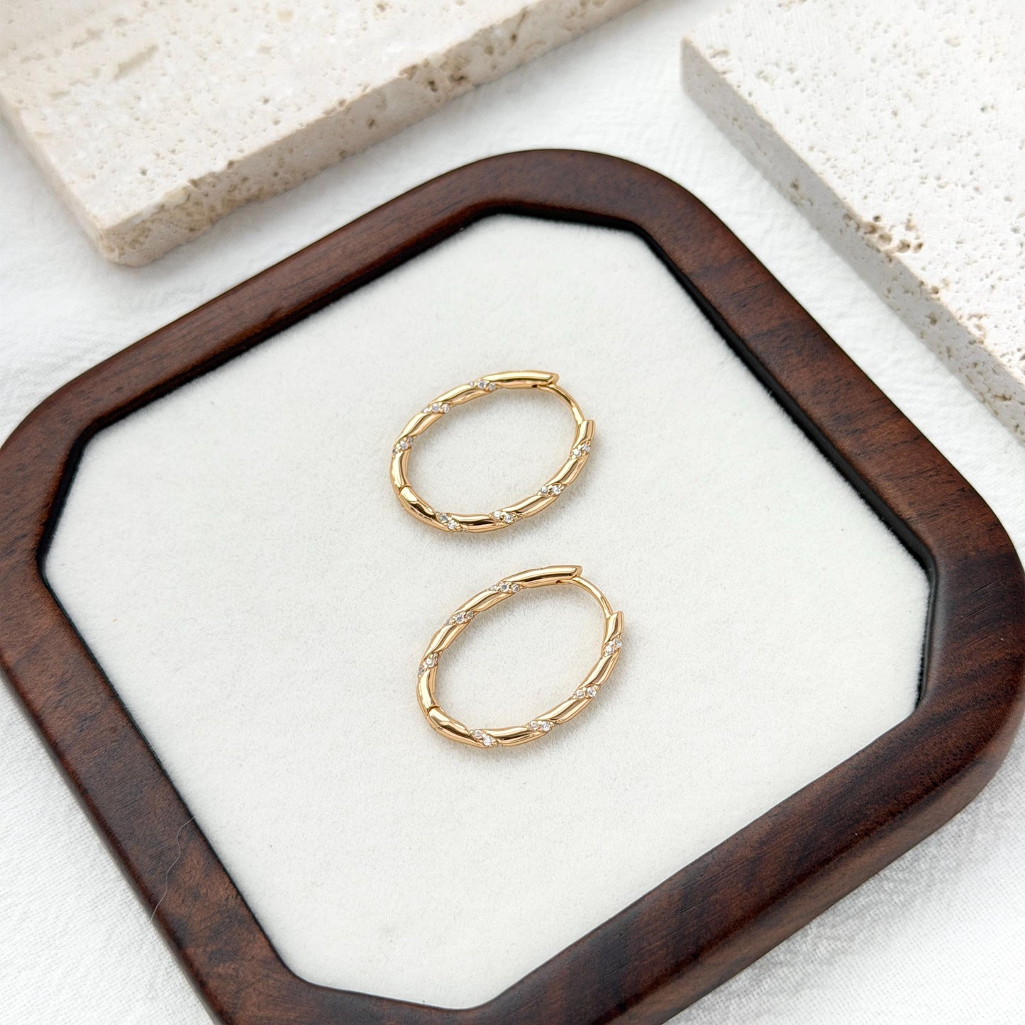 Gold hoop earrings on a white square pad inside a wooden frame.