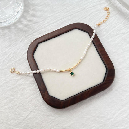Side view of 18K gold baroque pearl bracelet featuring a green zircon charm
