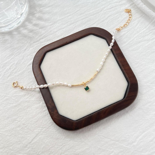 Side view of 18K gold baroque pearl bracelet featuring a green zircon charm
