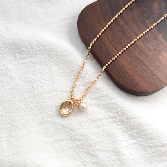 Close-up of 18K gold bean pendant and petite freshwater pearl, delicate handmade necklace.