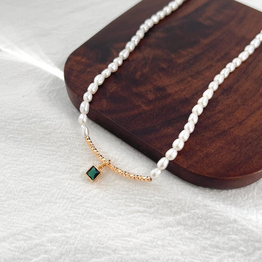 Close‑up of natural freshwater baroque pearls and tiny green zircon charm on 18K gold choker necklace, minimalist handcrafted.