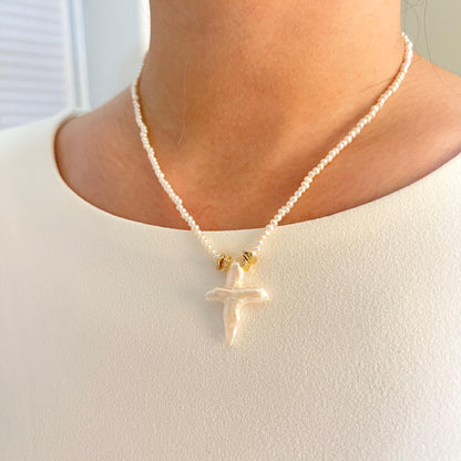 Pearl necklace with a gold pendant worn by a person against a neutral background