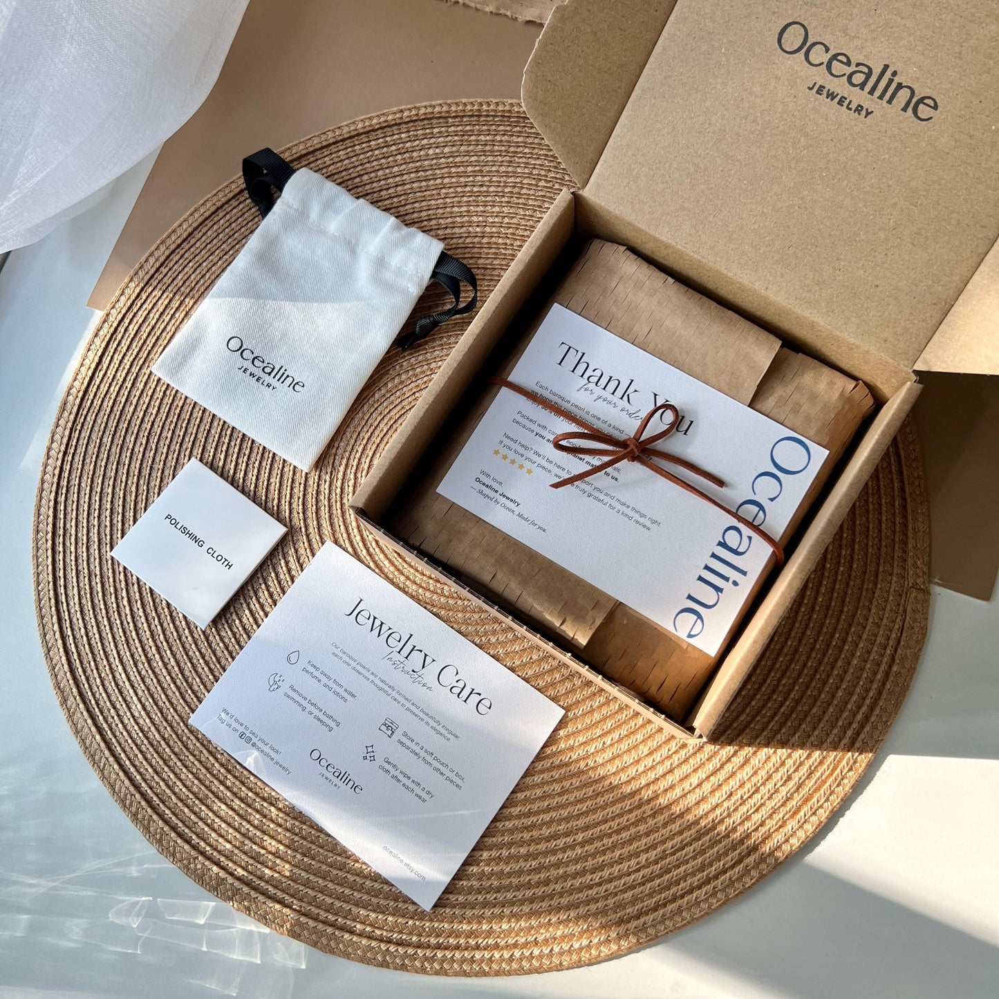 Ocealine jewelry packaging with a cardboard box, jewelry care card, and branded pouch on a woven mat.