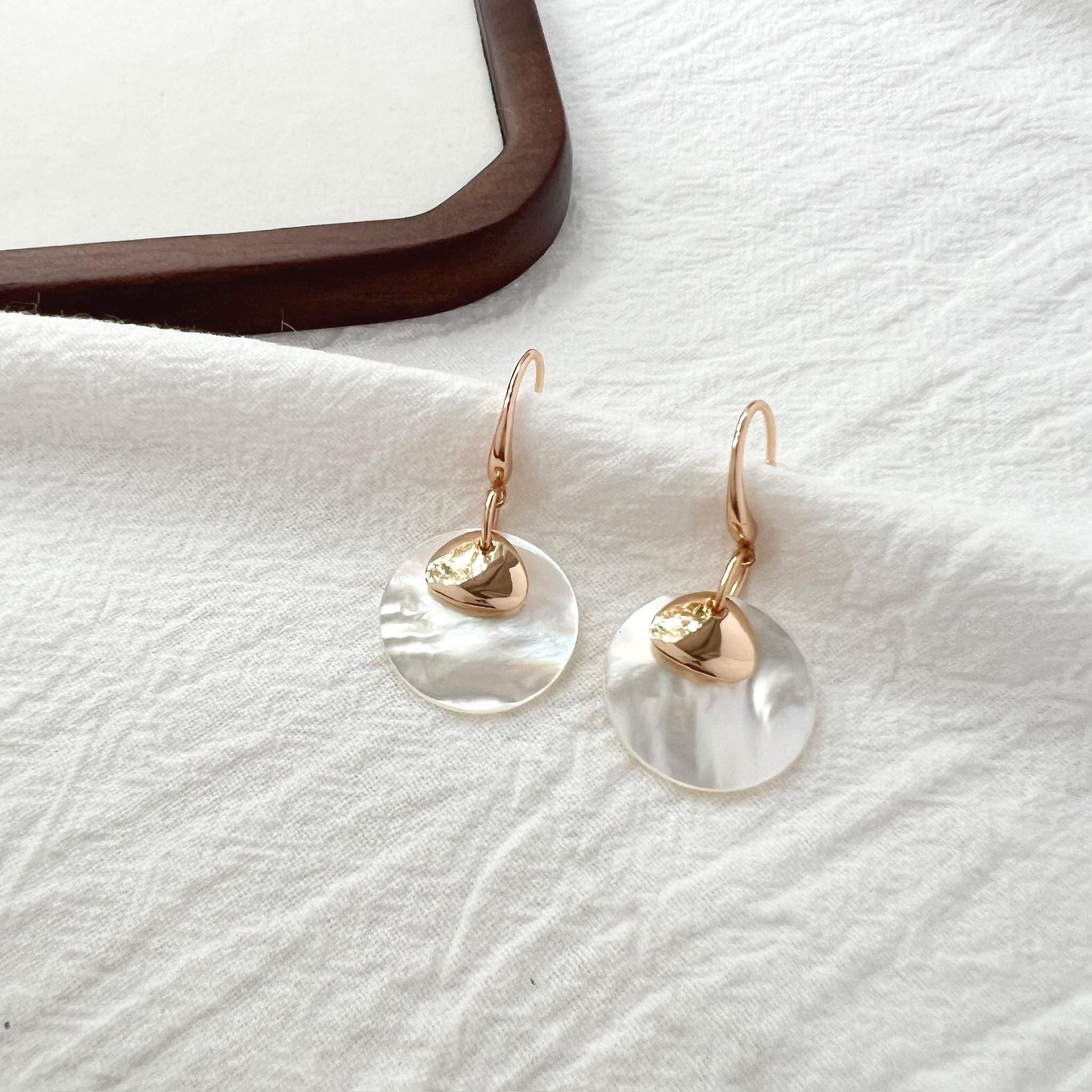 close up of 18k gold white mother of pearl dangling earrings texture and sheen
