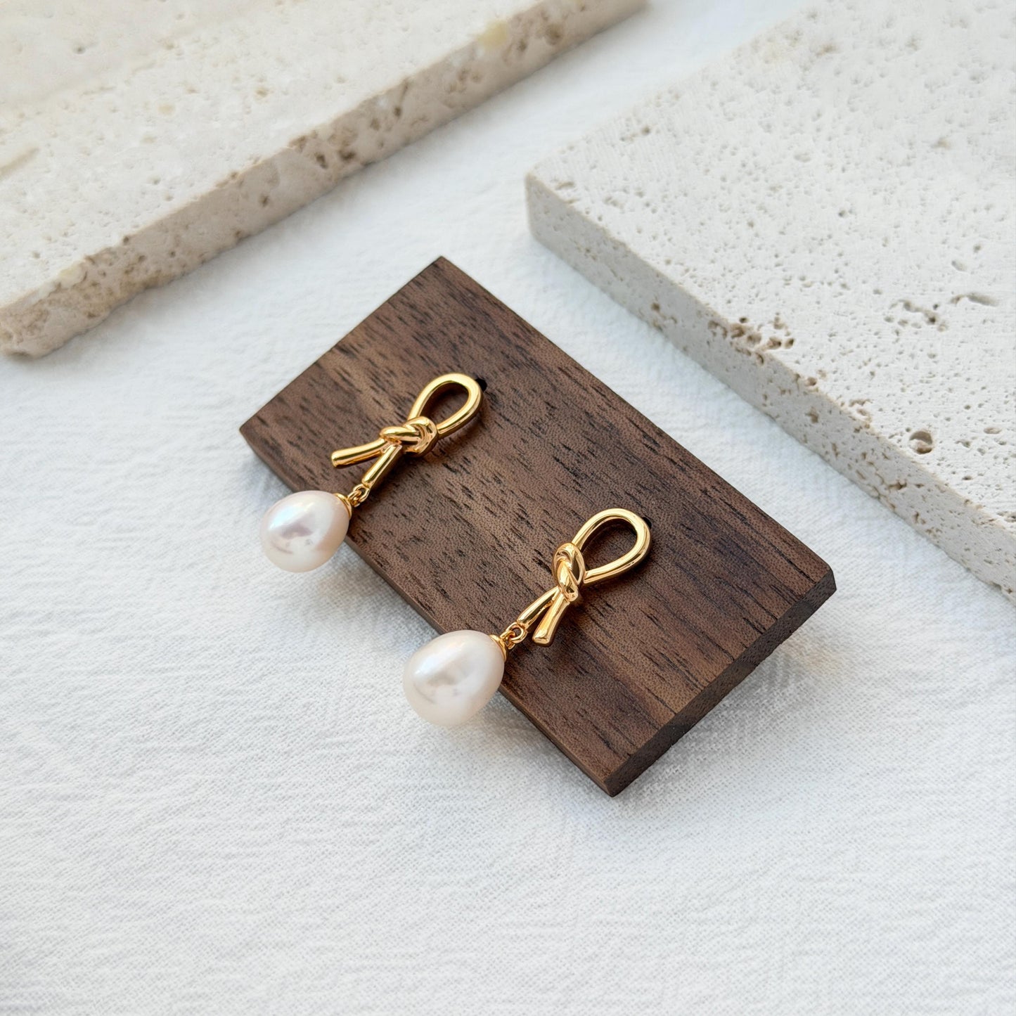 minimalist 18k gold bow pearl drop earrings styled flatlay jewelry
