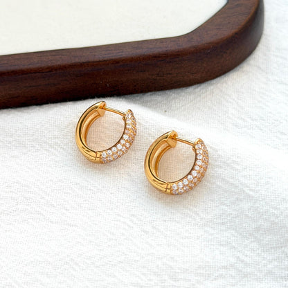 close up of 18k gold modern huggie hoop earrings with sparkling cubic zirconia
