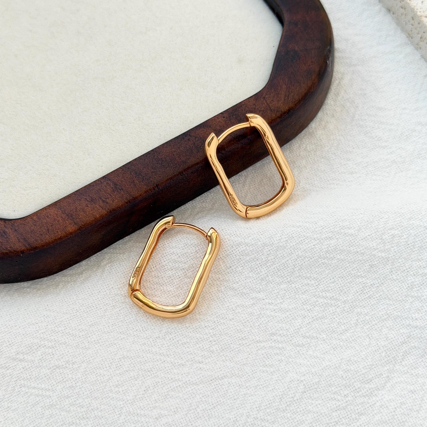 close up of 18k gold dainty rectangular huggie hoop earrings texture and detail

