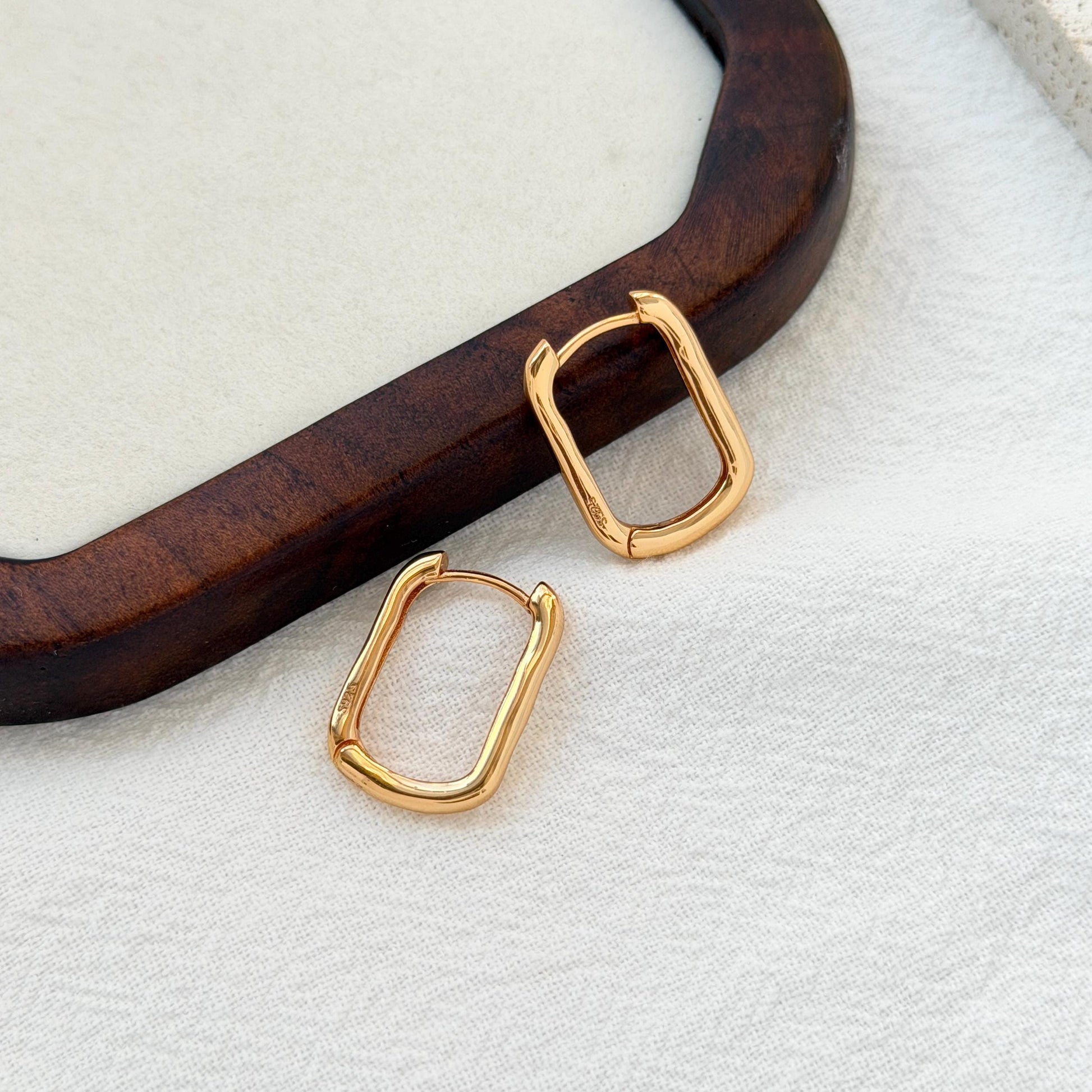 close up of 18k gold dainty rectangular huggie hoop earrings texture and detail
