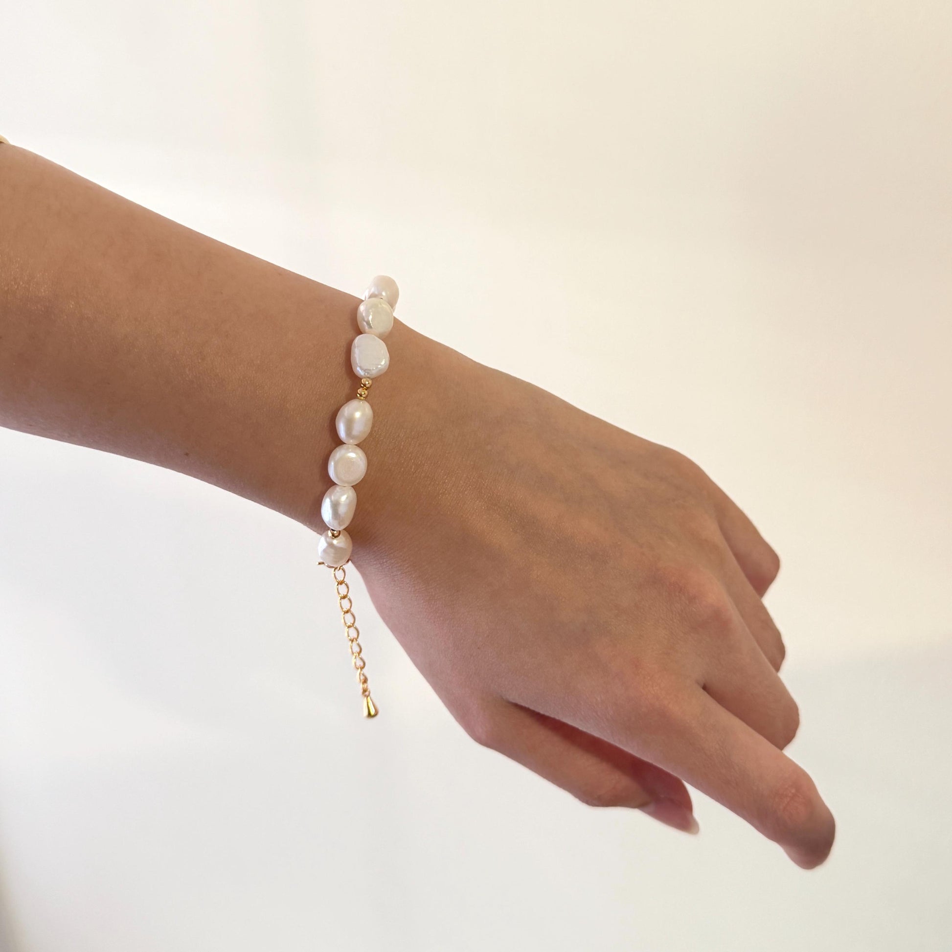 Hand wearing a pearl bracelet on a plain background