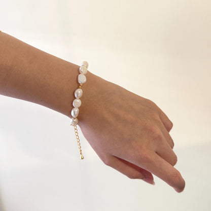 Hand wearing a pearl bracelet on a plain background