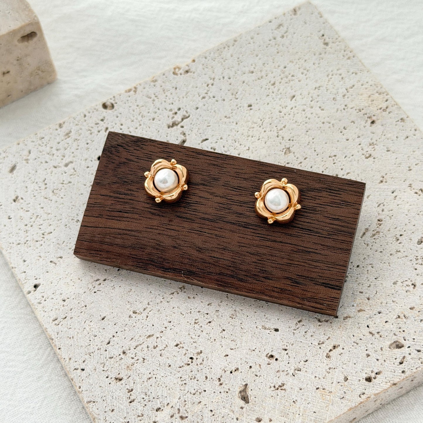 Gold freshwater pearl stud earrings shaped like small flowers, styled on a neutral jewelry display.
