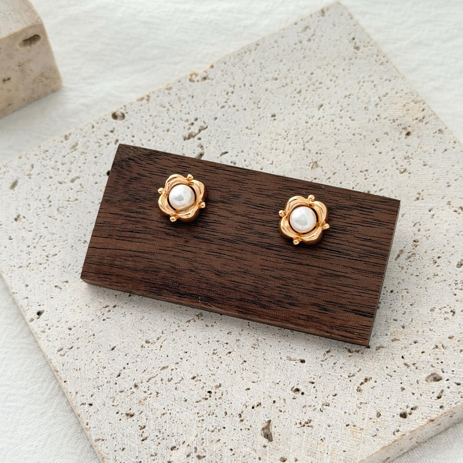 Gold freshwater pearl stud earrings shaped like small flowers, styled on a neutral jewelry display.
