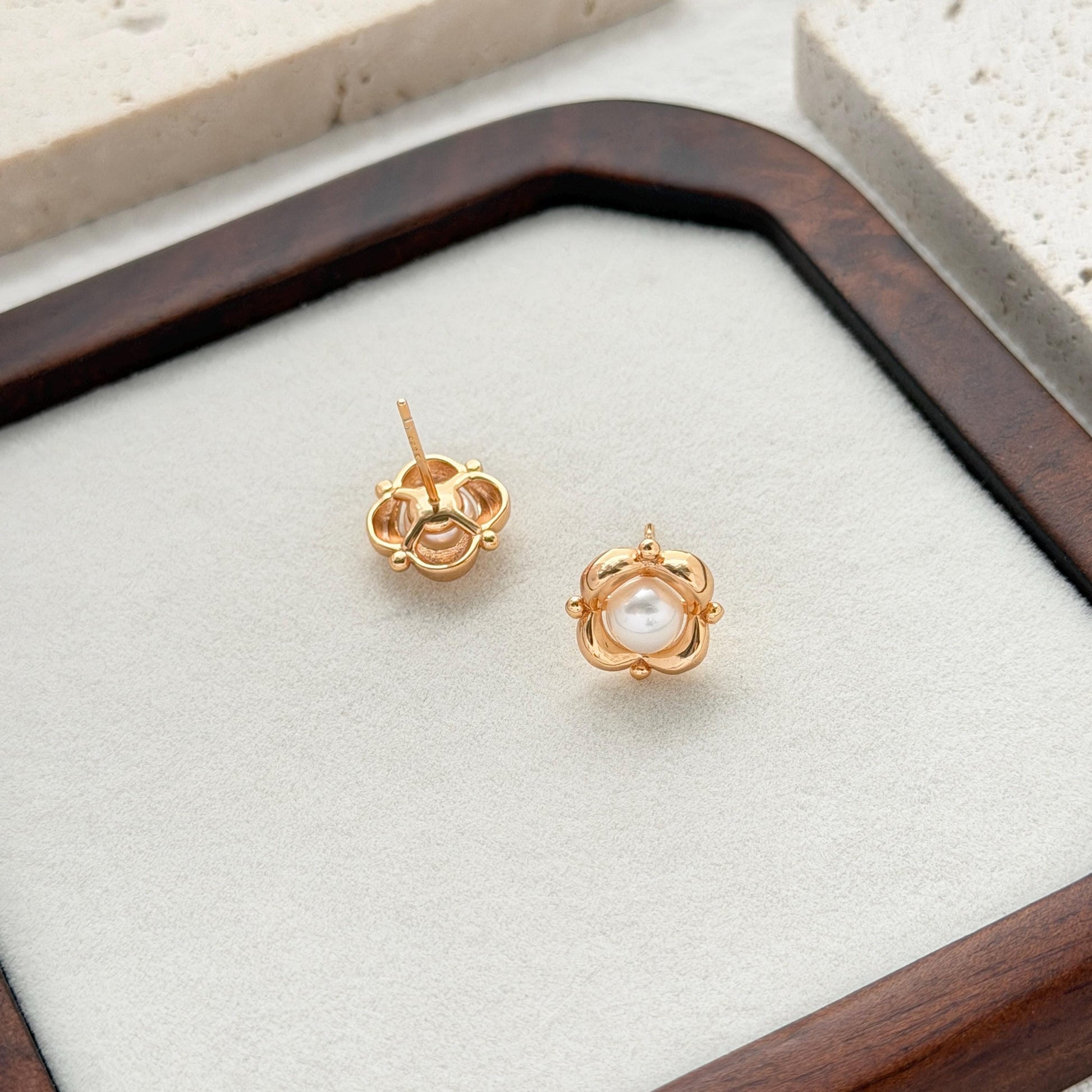 Statement pearl flower earrings displayed on a dark wooden jewelry tray with a minimalist background.
