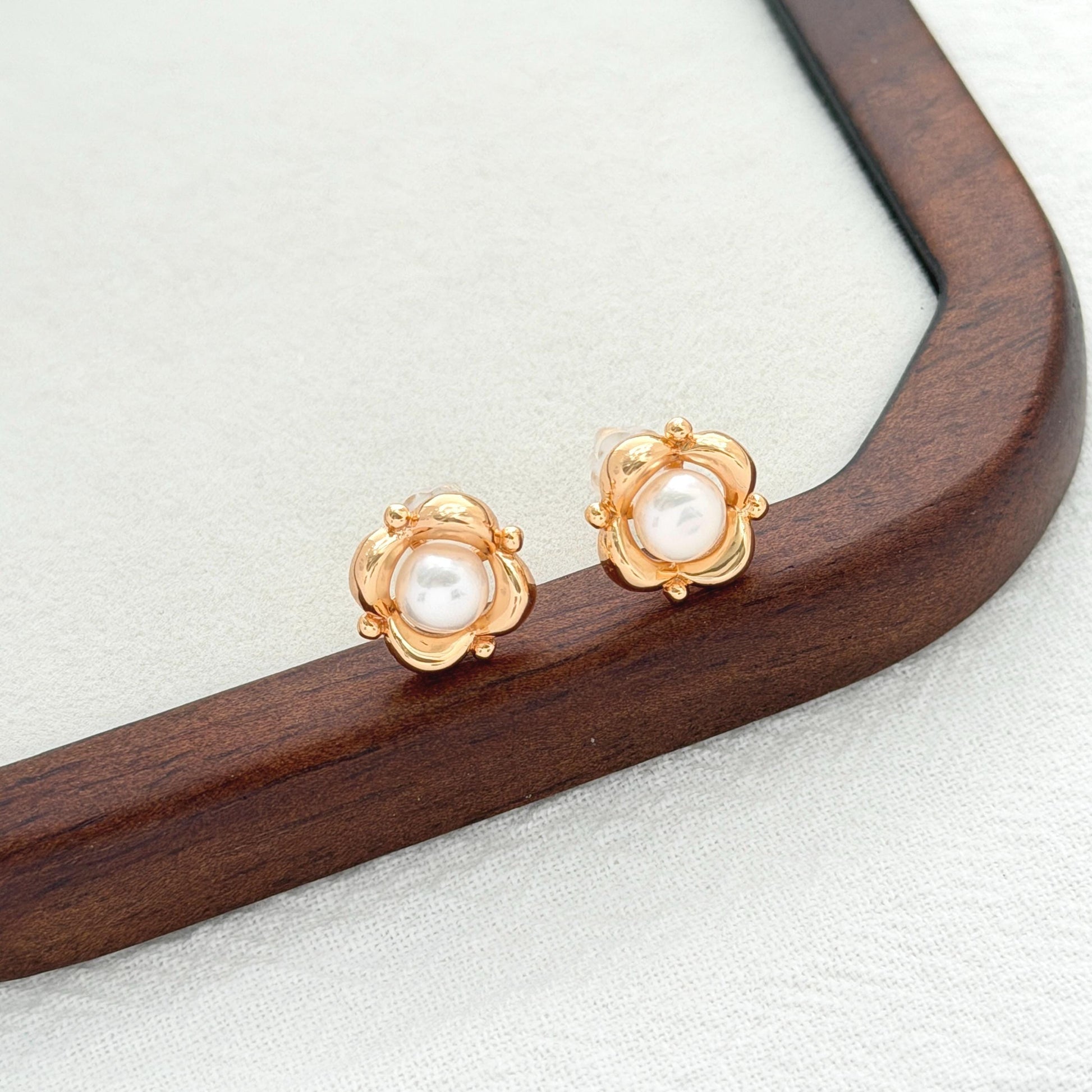 Vintage gold flower stud earrings with natural freshwater pearl centers on a dark wood display tray.