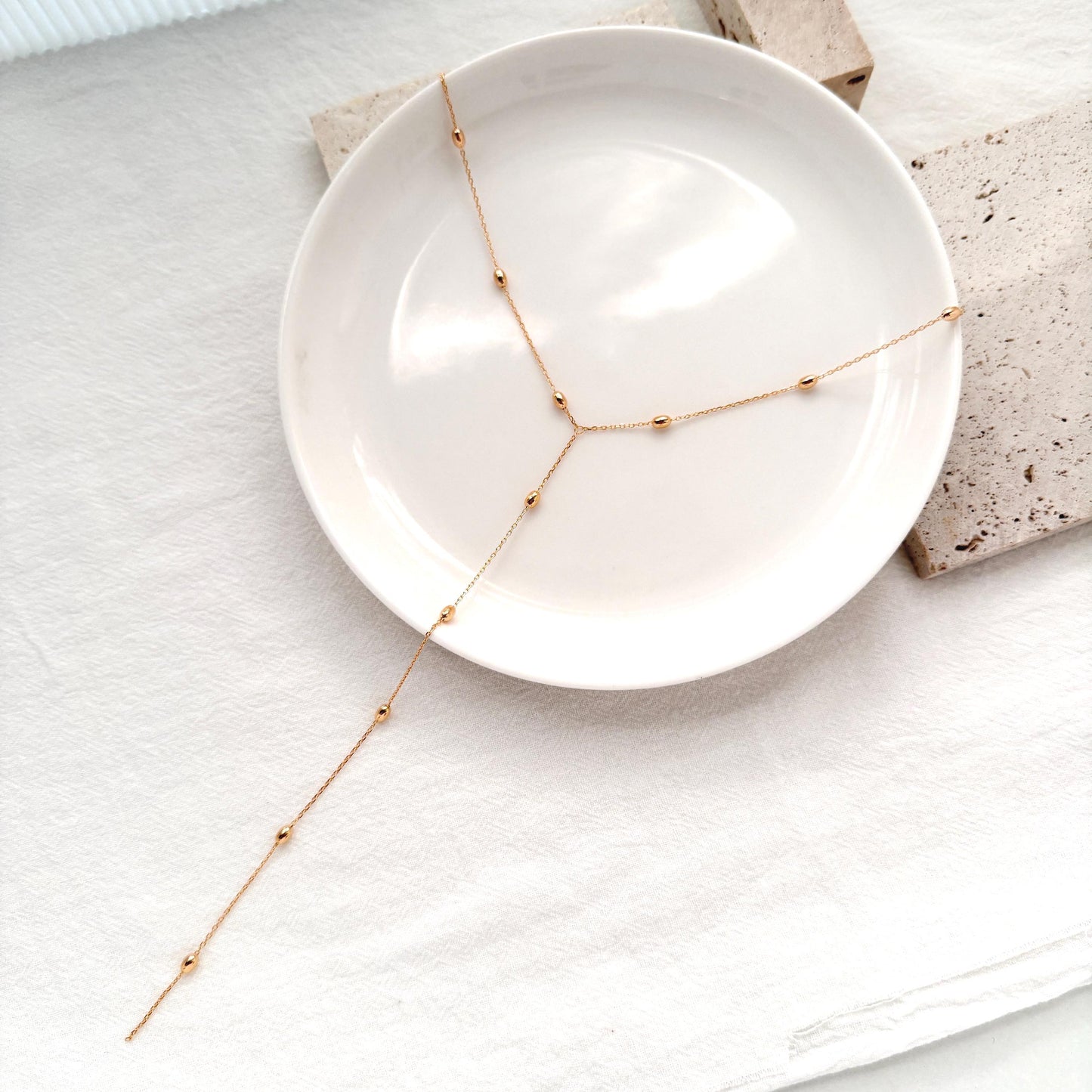Minimal gold lariat necklace featuring tiny polished bead accents and an adjustable chain.