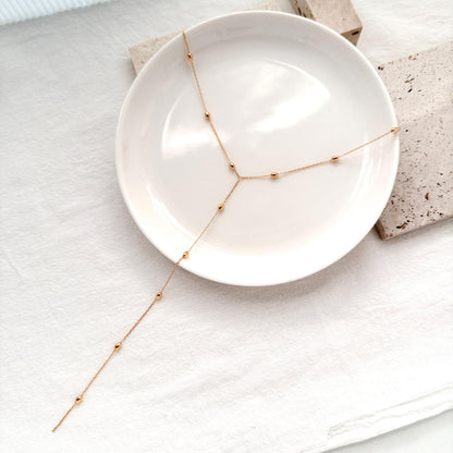 Minimal gold lariat necklace featuring tiny polished bead accents and an adjustable chain.