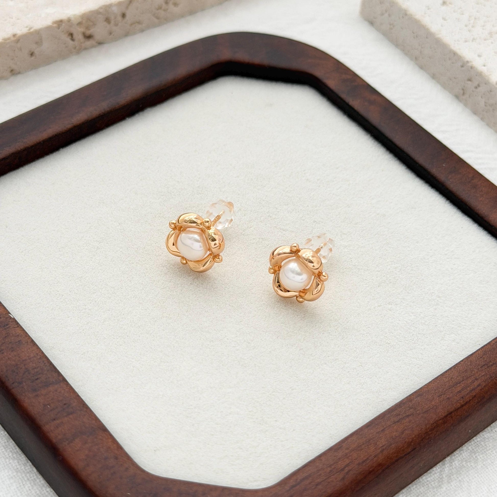 Elegant pearl flower stud earrings with a polished gold finish, photographed on linen and stone.