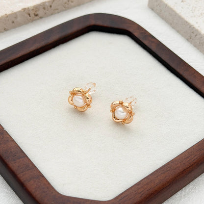 Elegant pearl flower stud earrings with a polished gold finish, photographed on linen and stone.