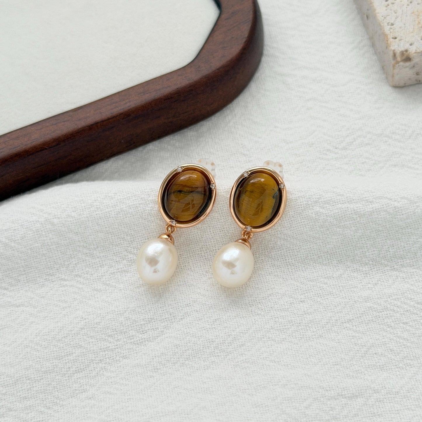 Vintage-inspired brown pearl earrings with polished tiger’s eye stones in oval gold frames.
