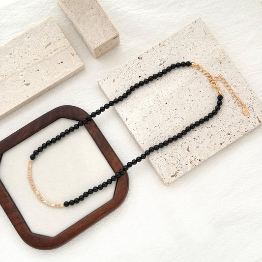 Black onyx necklace with small polished beads and warm gold accent details.