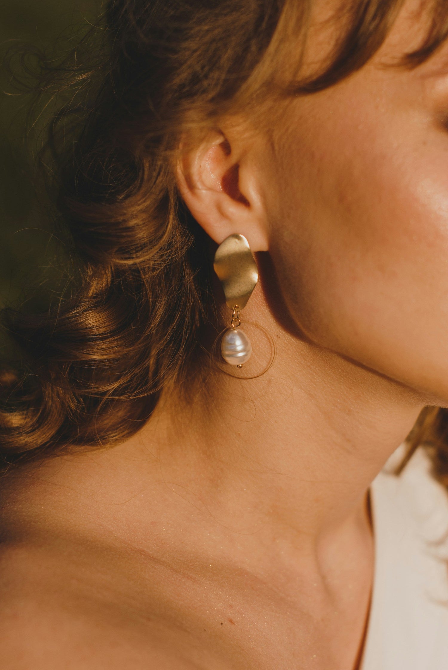 Close-up of a person wearing gold earrings with a pearl drop.
