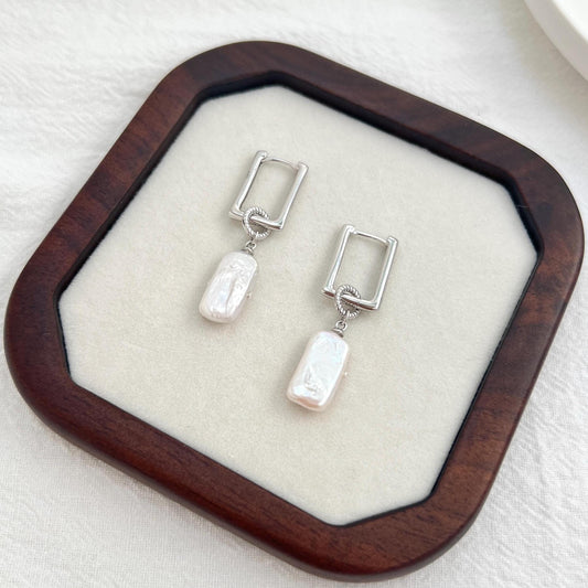 Close-up of silver rectangle baroque pearl dangle earrings highlighting texture of pearl and sleek silver hoop